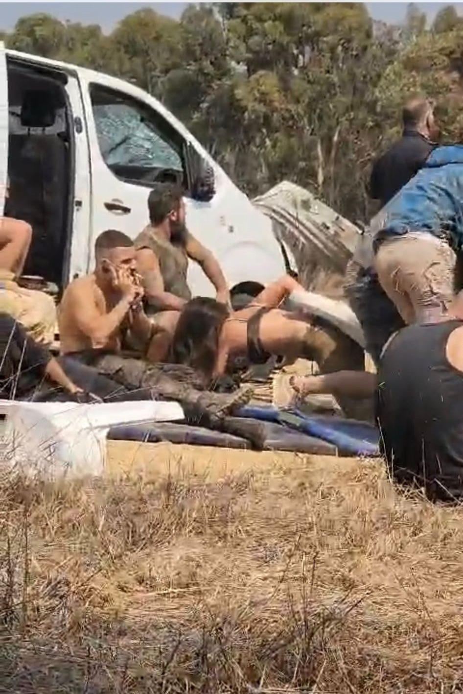 People hide behind a white van and sit on the ground