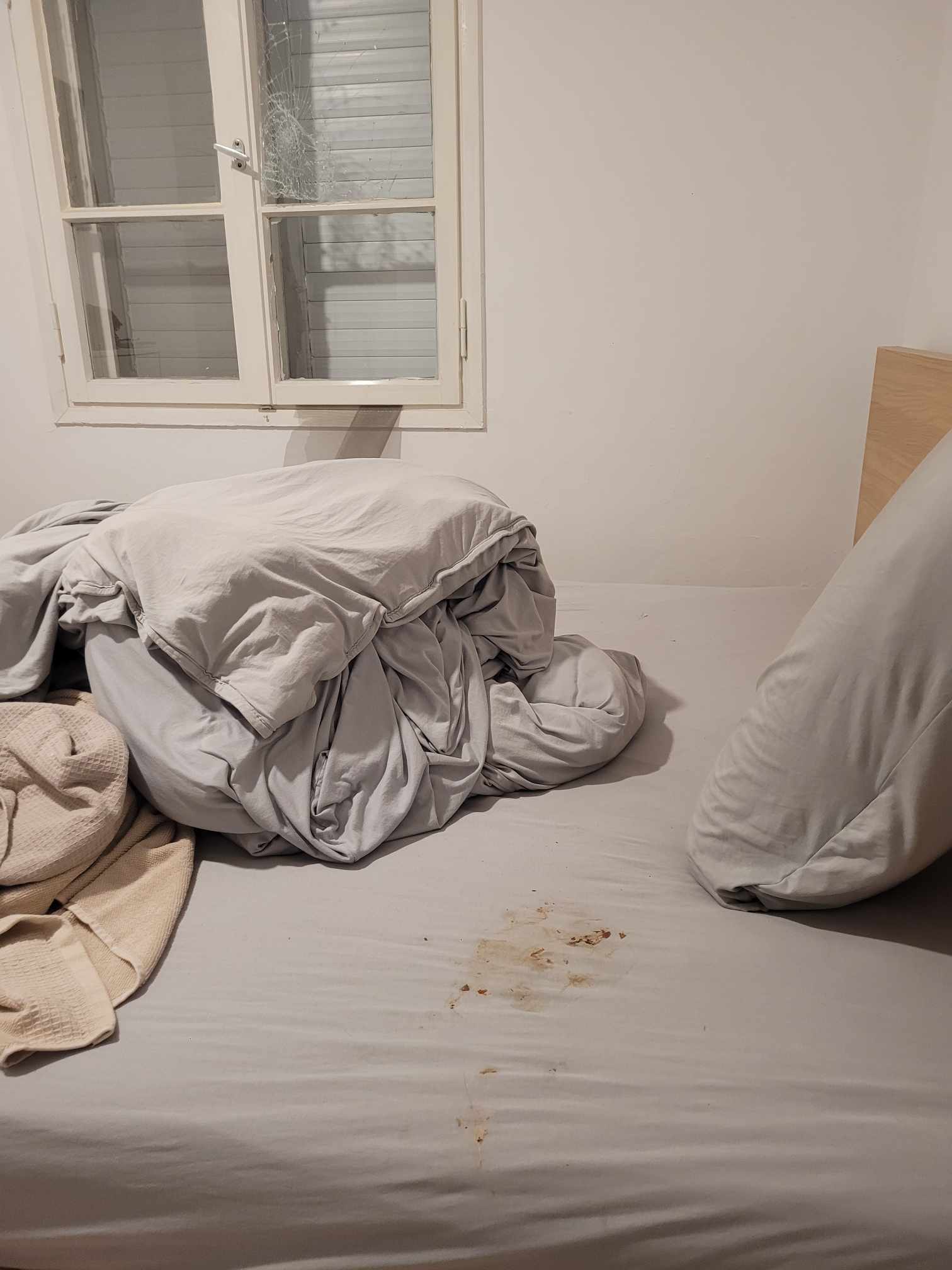 A bedroom with a broken window and blood stains on the sheets