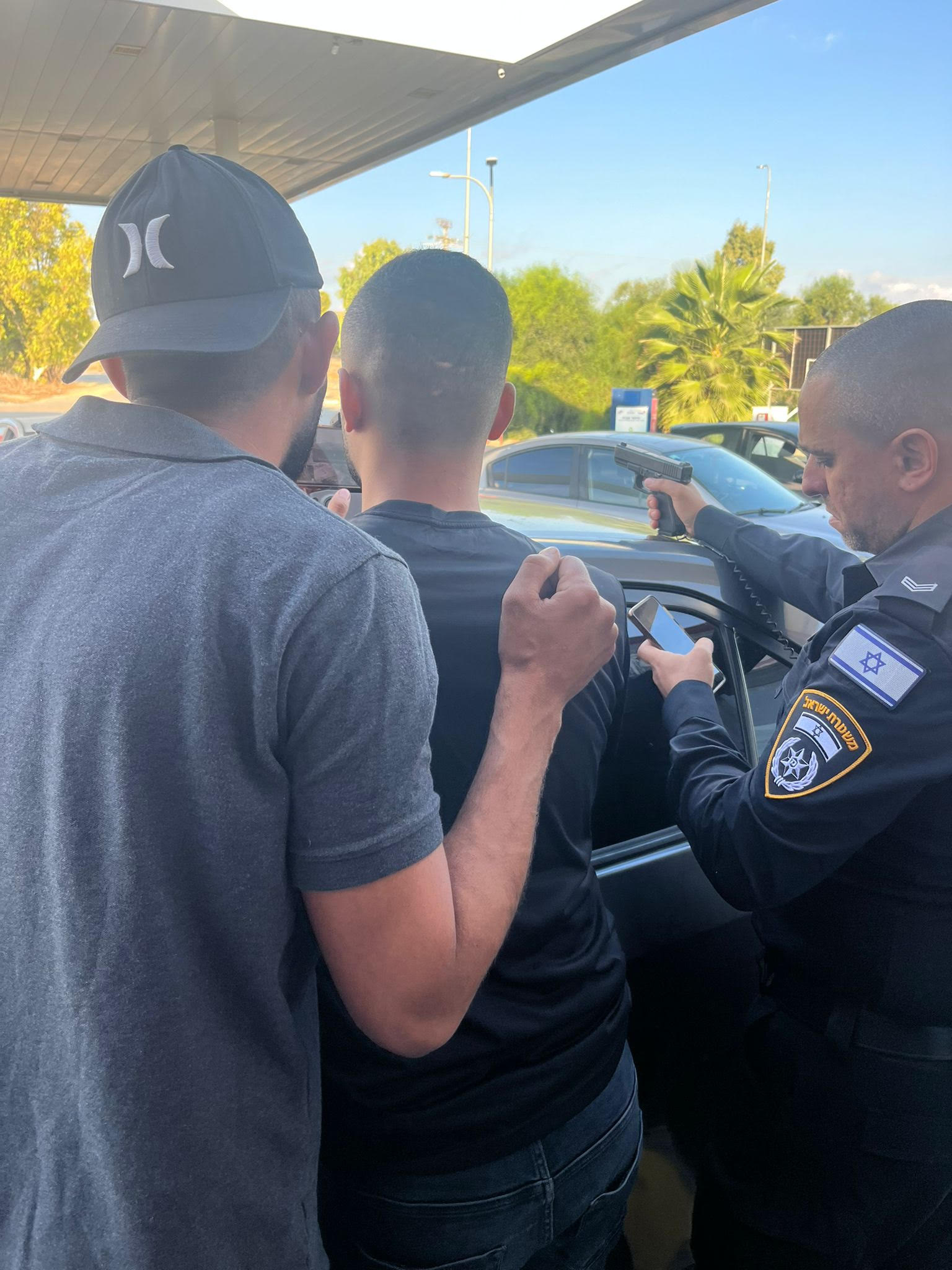 A policeman is holding a gun and two men are next to him