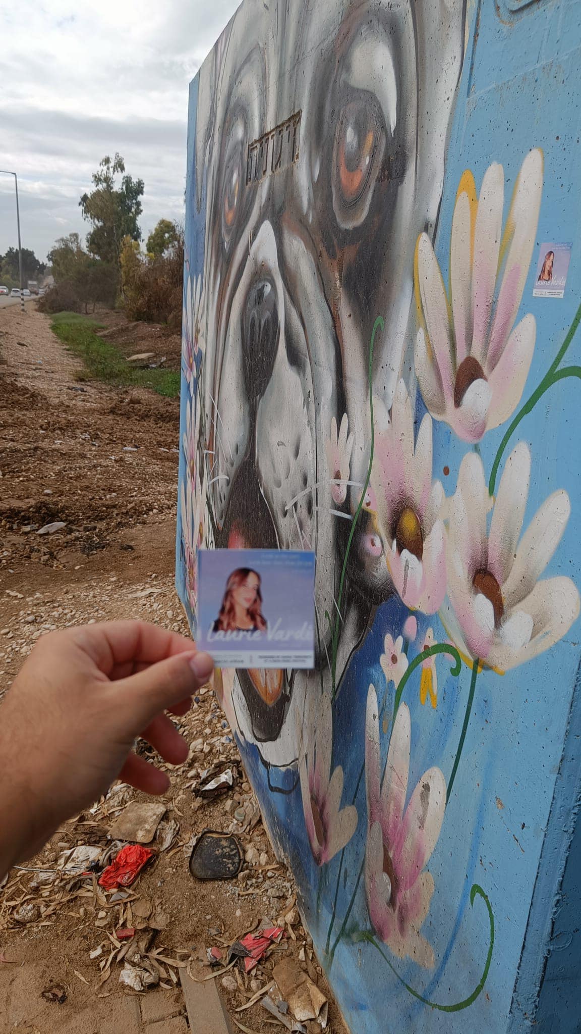In Nissim's hand there is a sticker with a picture of Laurie in front the shelter
