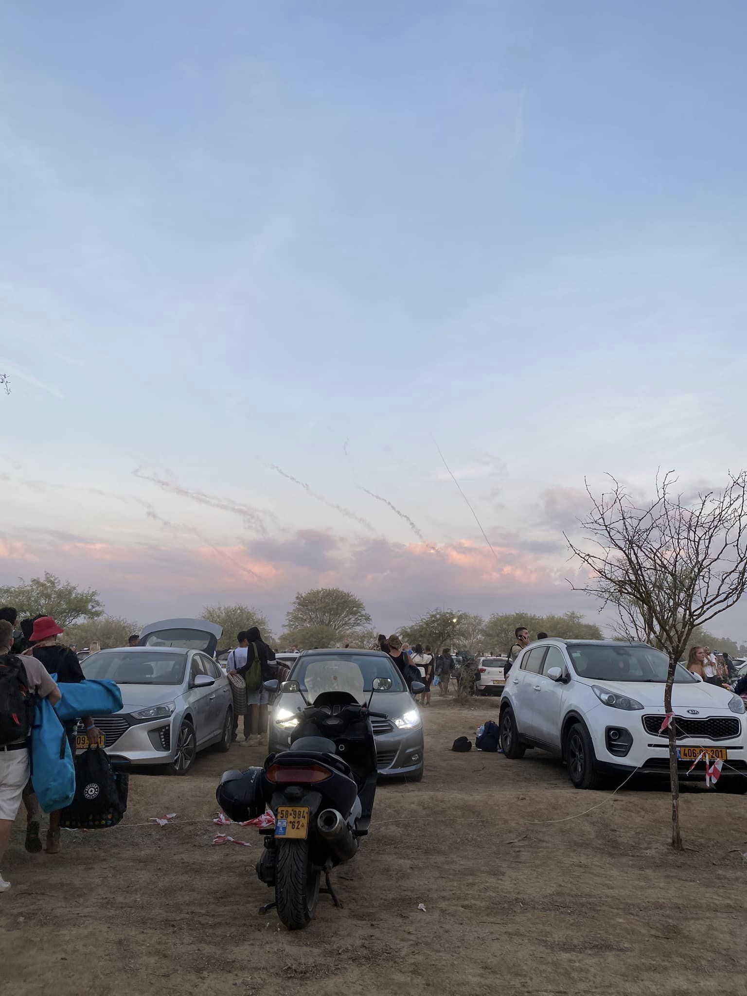 People are standing next to cars and above smoke marks in the sky