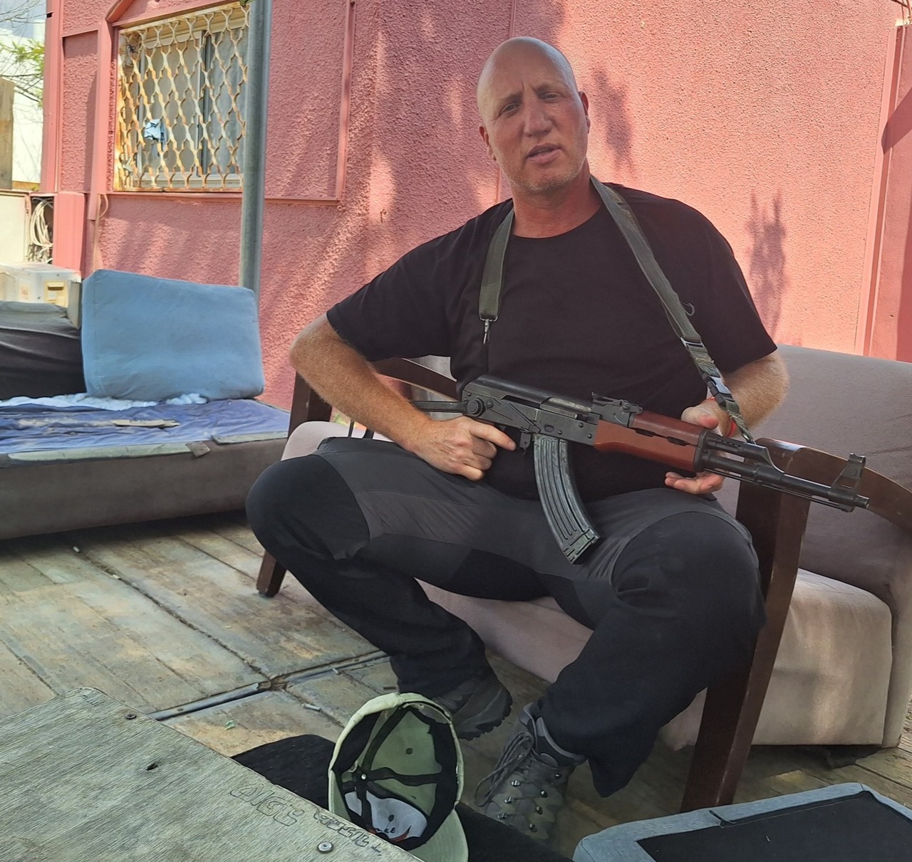 A man sits in an armchair and holds a Kalashnikov